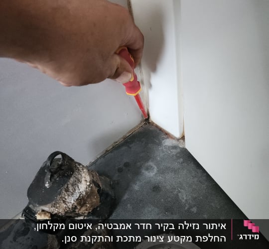 יד מחזיקה מברג ליד פינה עם רטיבות וניקוז